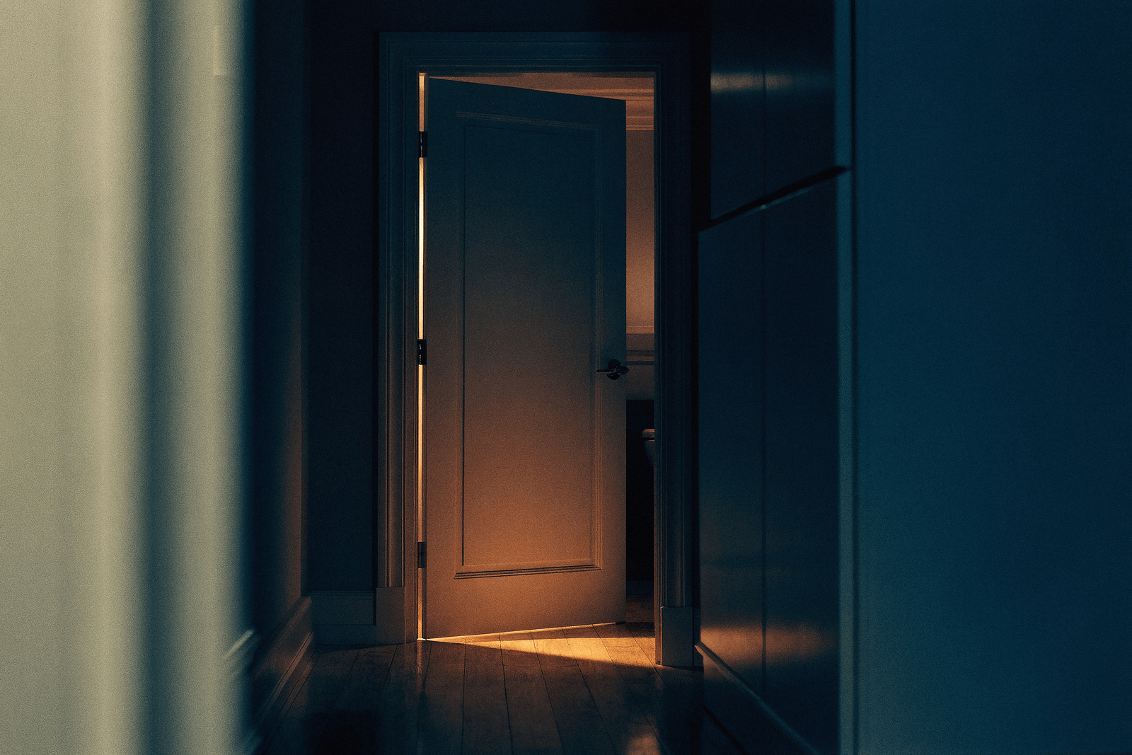 Porta de banheiro entreaberta à noite com luz quente acesa em um corredor escuro · acordar de madrugada para urinar